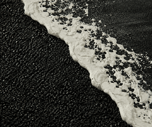 Foamy white ocean wave on black sand beach wall art, textured photographic print for modern decor.
