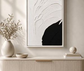 Minimalist sideboard with ceramic vases, green plant, and black and white abstract wall art above.