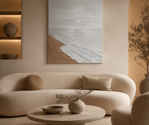 Wallsmark INC Blush Coast Seascape Wall Art above curved sofa, round table, and pottery in minimalist living room.