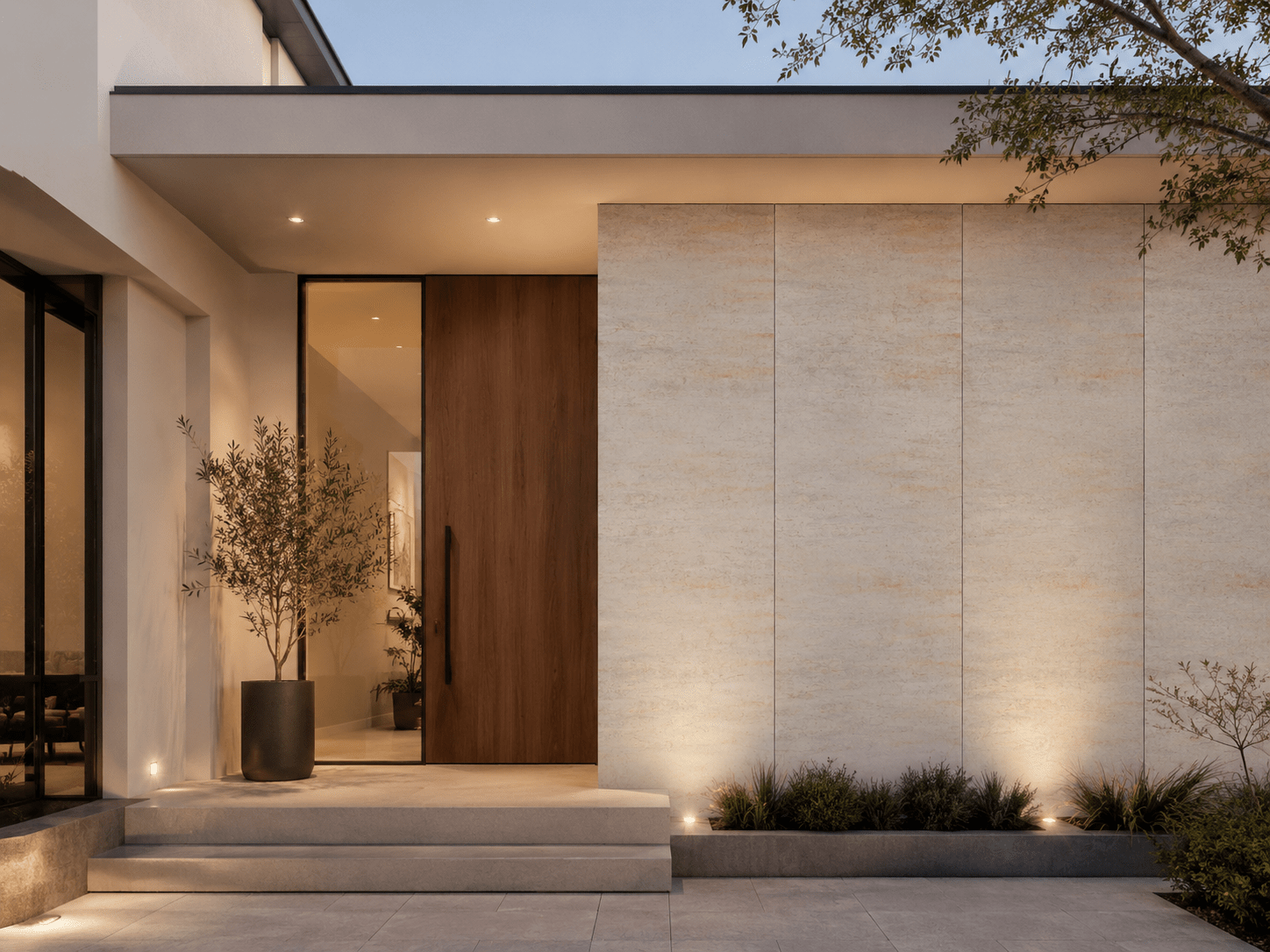 Modern house entrance with a large wooden door, beige stone walls enhanced by elegant Gold Travertine wall cladding, recessed lighting, a potted plant on the left, and neatly trimmed shrubs along the front walkway at dusk.