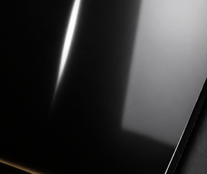 High-gloss black wall panel with reflective finish, showing light, window reflection, and a scratch near the center.
