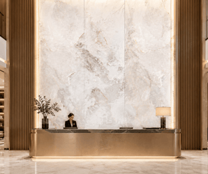 Gold reception desk with marble floor, decorative wall panels, table lamp, vase with branches in hotel lobby.