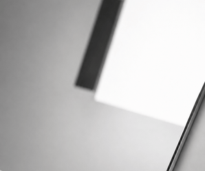Rectangular polished silver mirror wall panel on gray surface reflecting white square and black rectangle shapes.