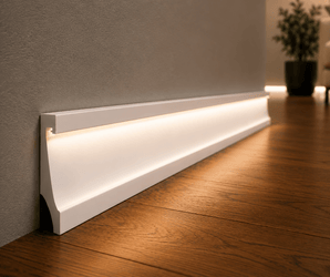 Baseboard LED strip lighting installed along brown wood flooring and gray wall in a living room setting.